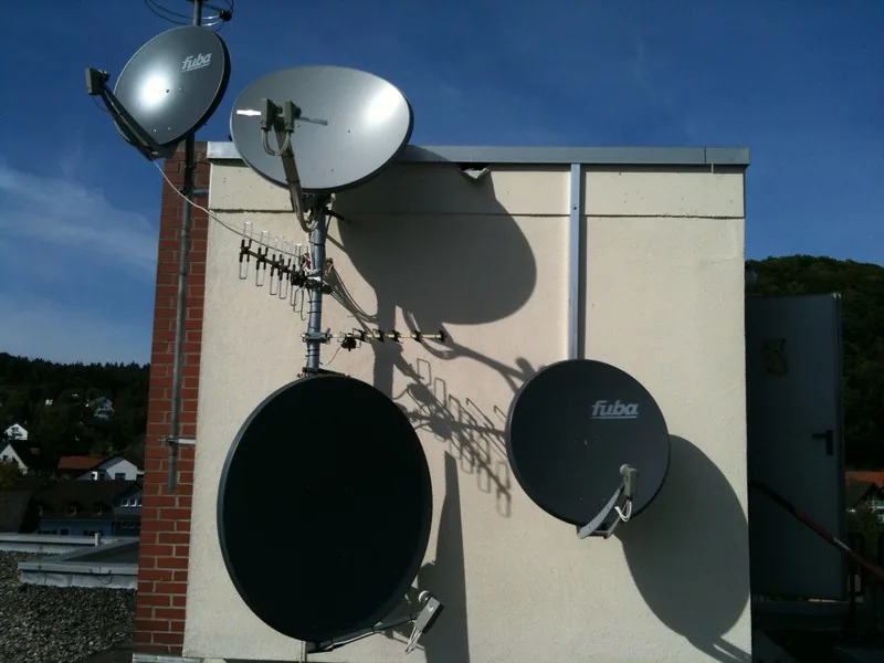 Mehrere Satellitenschüsseln und eine Terrestrik-Antenne an einer Hauswand