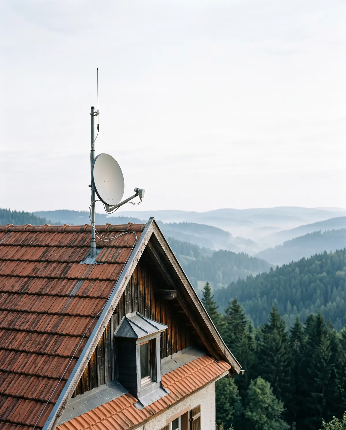 Satellitenschüssel und Antennenmast am Giebel eines Schwarzwaldhauses