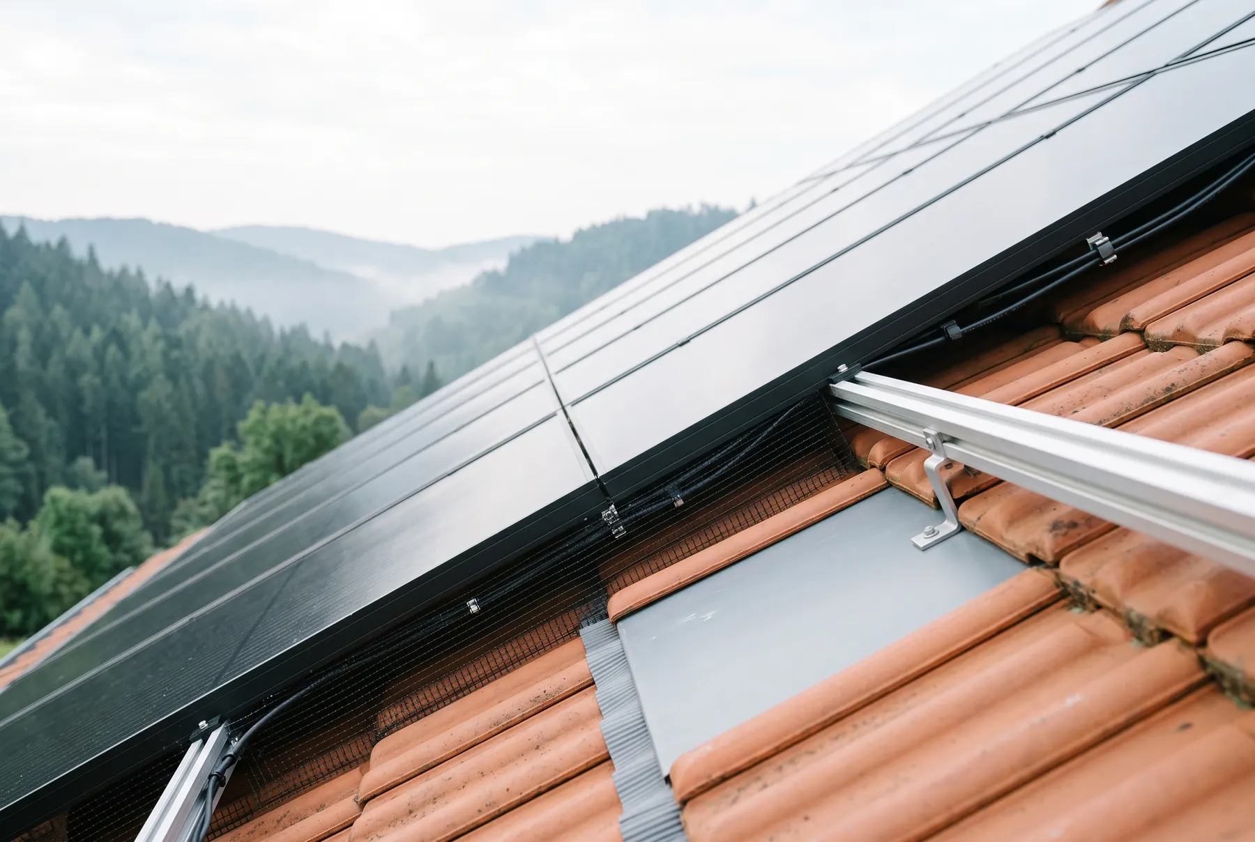 Schwarze Solarmodule auf einem Ziegeldach, unter der Schiene eine Metalldachplatte anstelle eines Dachziegels